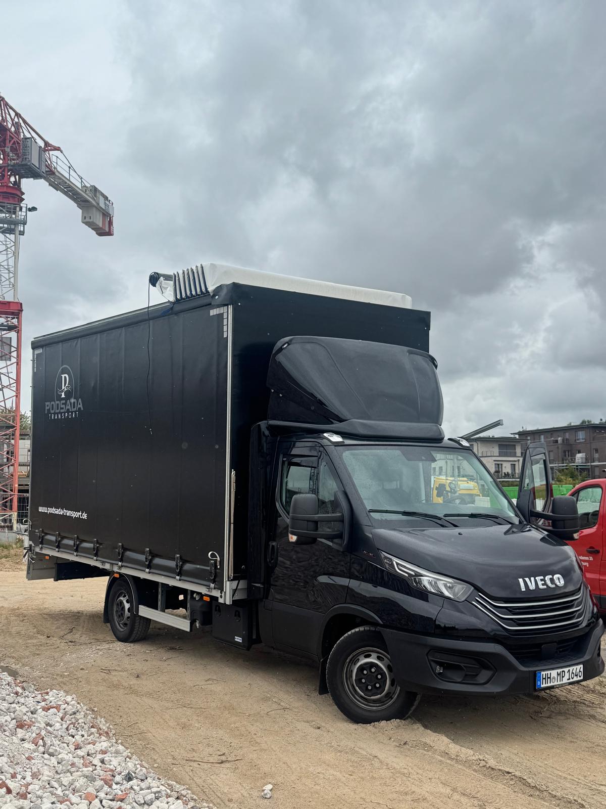 Ciężarówka IVECO Podsada Transport na placu budowy z żurawiem wieżowym w tle
